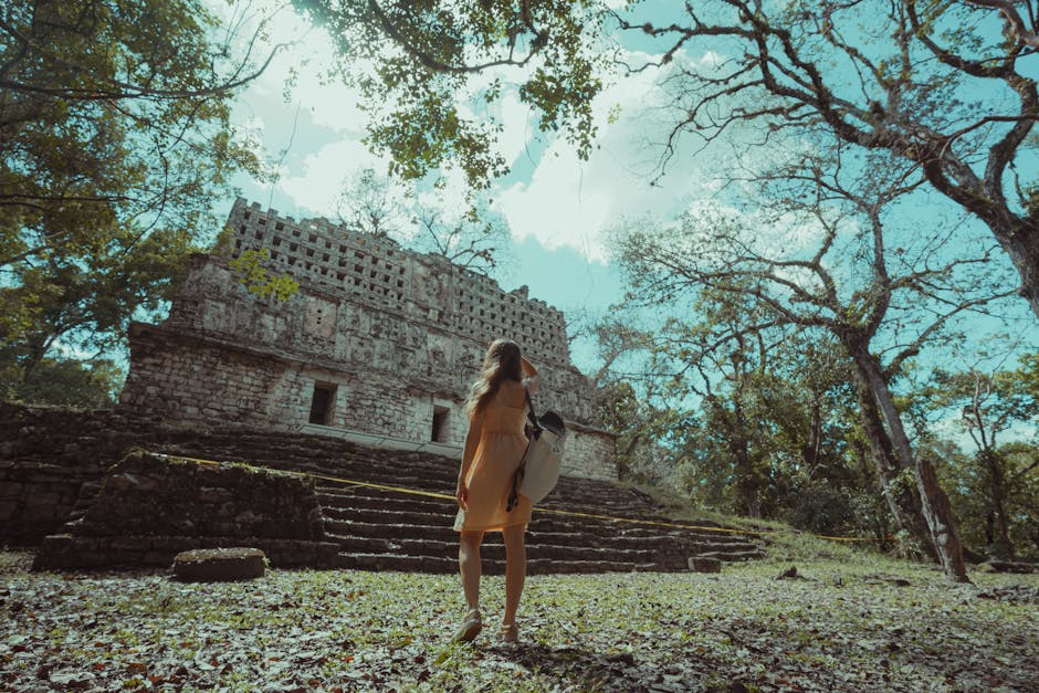 A woman stands before ancient Mayan ruins in a tranquil forest setting in Mexico.